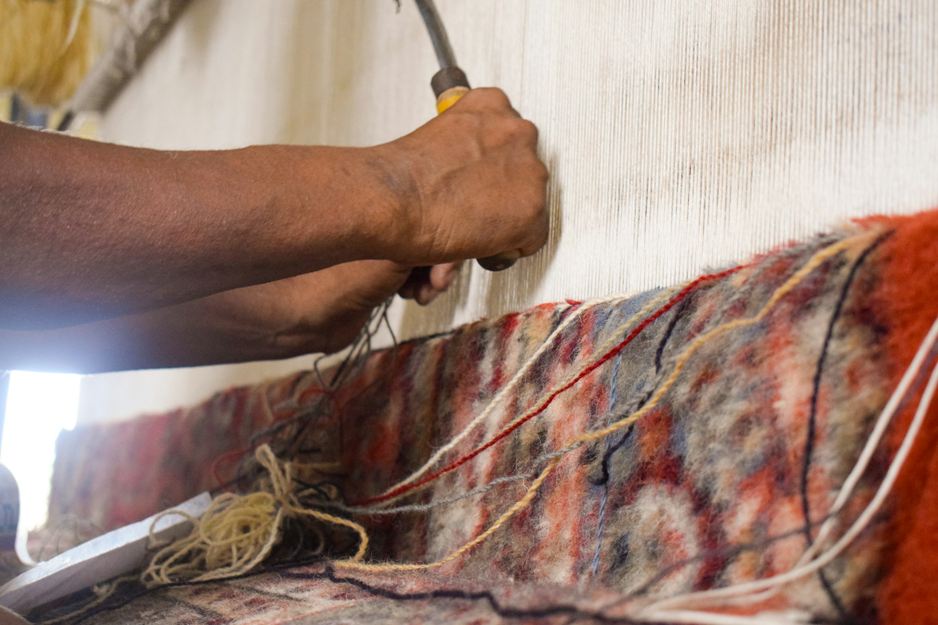 A person weaving a colorful carpet with a tool